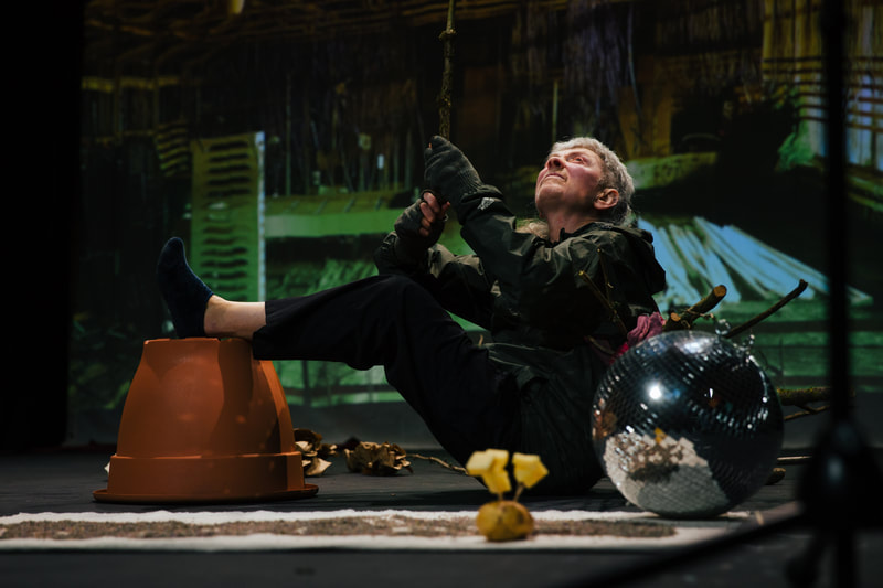 a woman balancing her legs up on a giant plant pot surrounded by glitter balls looks upwards